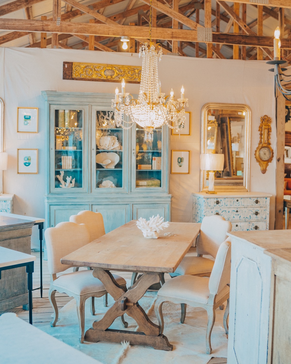 A soft-blue painted china cabinet and crystal chandelier above a trestle dining table