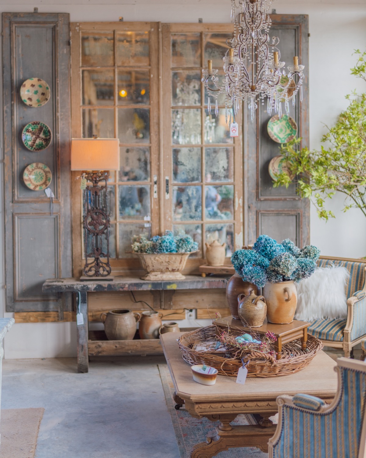 Antique French doors, a chandelier, and blue hydrangeas in a styled vignette