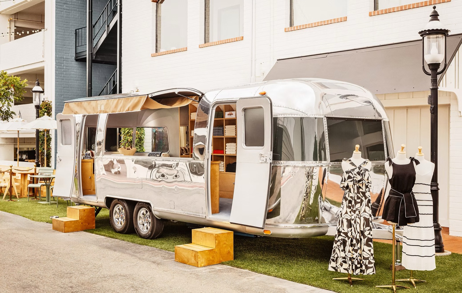 Sézane's polished-silver 'En Route' Airstream trailer parked outside a white storefront, with dresses displayed on mannequins beside it